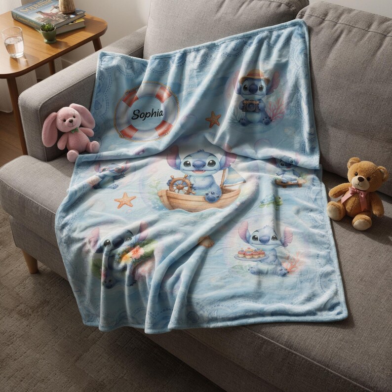 May include: A light blue fleece blanket featuring a repeating pattern of the character Stitch in various nautical scenes, including a life preserver with the name Sophia printed on it, a wooden boat, and a tray of cupcakes, all on a soft fabric.