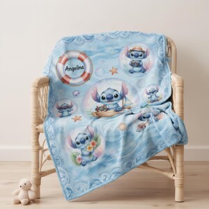 May include: A light blue fleece blanket featuring a repeating pattern of the character Stitch in various nautical scenes, including bubbles, seashells, starfish, and a life preserver ring with the name Angelina printed in black text.