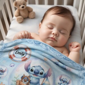 May include: A light blue baby blanket featuring a graphic of the character Stitch steering a wooden ship wheel, a life preserver ring with the name Emily printed in black text, and small seashells, covering a sleeping infant and a teddy bear.
