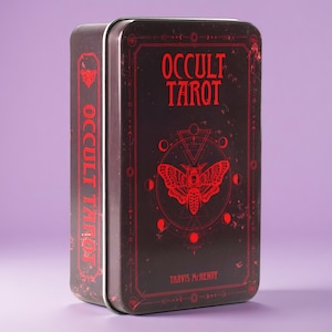 May include: A rectangular black metal tin featuring the text OCCULT TAROT in red lettering. The front displays a red moth illustration centred within geometric shapes and lunar phases. The side also features the text OCCULT TAROT in red.