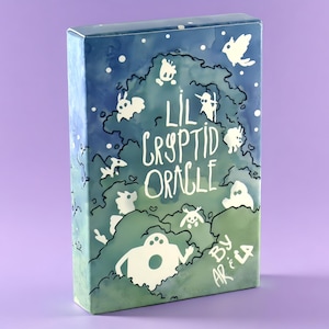 Peut inclure: Une boîte de jeu rectangulaire pour le Lil Cryptid Oracle par Ariela, avec un dégradé de style aquarelle allant du bleu au vert. Le devant présente des silhouettes blanches de diverses créatures et le texte Lil Cryptid Oracle by Ariela.