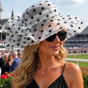 Puede incluir: Un sombrero blanco de ala ancha hecho de tela transparente y ligera con un patrón de lunares negros. El sombrero incluye un gran lazo decorativo con volantes en el lateral, una copa redondeada y un ala estructurada que se curva ligeramente hacia abajo.
