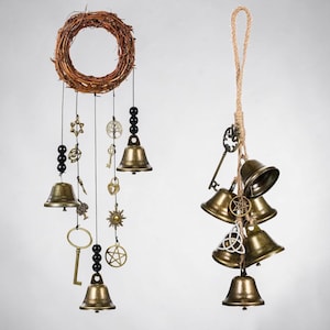 May include: A hanging decoration featuring a circular twig wreath with dangling brass bells, black beads, and metal charms including keys, a star, and a tree. Beside it, a jute rope holds a cluster of brass bells and various metal charms.