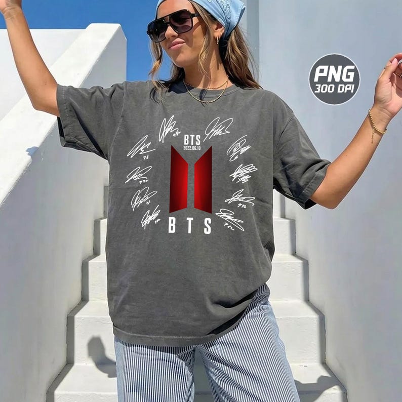 May include: A charcoal grey short-sleeve t-shirt featuring a central red and black BTS logo with the text BTS 2022.06.10. The design is surrounded by a circular arrangement of white printed signatures on the front of the garment.