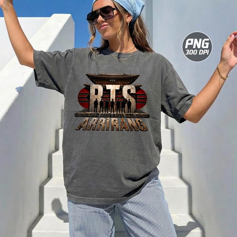 May include: A charcoal grey short-sleeve t-shirt featuring a graphic print of a traditional East Asian architectural structure with the text BTS and ARIRANG, along with silhouettes of seven figures standing in front of a large red circular background.