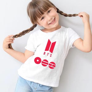 May include: A white short-sleeved t-shirt featuring a red graphic print on the chest. The design includes the red BTS logo above the text BTS and three red circular icons containing geometric shapes and the letters O, E, and H in white.