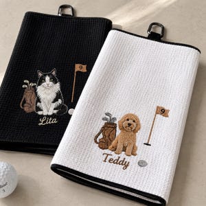May include: Two waffle-textured golf towels, one black and one white, each featuring an embroidered golf bag, a flag with the number 9, and a pet. The black towel shows a black and white cat with the name Lita, while the white towel shows a brown dog with the name Teddy.