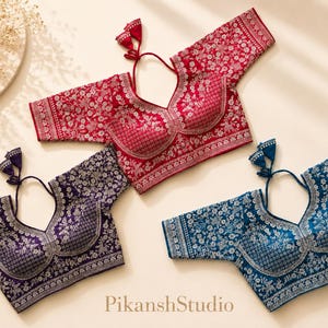May include: Three short-sleeved blouses in red, deep purple, and blue, each featuring intricate silver floral embroidery, a sweetheart neckline, and a back tie closure with tassels. The text PikanshStudio is printed at the bottom center.