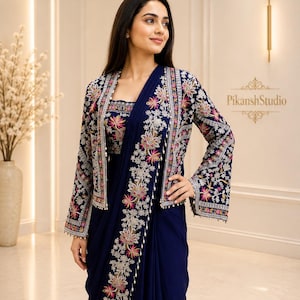 May include: A deep navy blue ensemble featuring a sleeveless bodice and a matching long-sleeve jacket. Both pieces are adorned with intricate floral embroidery in shades of pink, white, and gold. The jacket has flared sleeves and a straight hem.