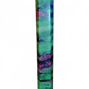 Puede incluir: Un obelisco alto de piedra preciosa pulida. El obelisco es principalmente verde con vetas moradas, negras y rojas. La parte superior es de color rojo intenso. Está montado sobre una base marrón. Es un objeto decorativo.
