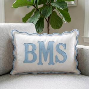 May include: A rectangular white throw pillow featuring a light blue scalloped edge trim and the embroidered letters BMS in a large, light blue serif font centered on the front. The pillow has a smooth fabric texture and a clean, finished look.