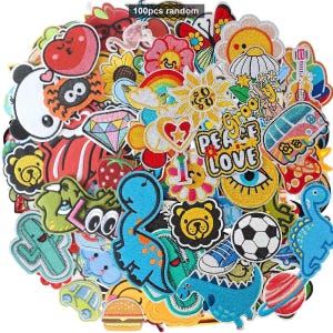 May include: A collection of 100 assorted embroidered fabric patches featuring colourful designs including dinosaurs, flowers, a football, a hamburger, a planet, a van, and text reading Peace Love. The patches are arranged in a dense, overlapping pile.