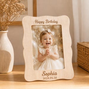 Peut inclure: Un cadre photo en bois clair aux bords ondulés portant l'inscription gravée Happy Birthday en haut et le nom Sophia avec la date 2024.05.20 en bas, contenant une photographie d'un enfant souriant vêtu d'une robe blanche.