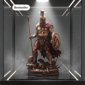 May include: A detailed Spartan warrior figurine standing on a circular base, wearing a crested helmet, chest armor, and a red cape. The figure holds a tall spear and a round shield, with a second helmet resting on the ground. Text reads Bestseller.