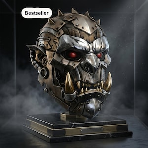 May include: A metallic orc head sculpture featuring glowing red eyes, prominent tusks, and mechanical gear details. The head is mounted on a rectangular black marble base with a gold-toned plaque. A white tag with the text Bestseller is visible.