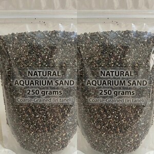 Könnte beinhalten: Ein durchsichtiger, wiederverschließbarer Kunststoffbeutel gefüllt mit grobkörnigem, natürlichem Aquariensand. Das Etikett lautet: NATURAL AQUARIUM SAND, 250 grams, Coarse-Grained (iri taneli). Der Sand besteht aus kleinen, dunklen, bunten Steinchen.