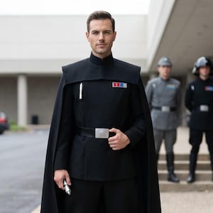 May include: A black military-style uniform featuring a high-collared tunic, a matching floor-length cape, and black trousers. The outfit includes a black belt with a silver buckle, a rank badge with red and blue squares, and tall black boots.
