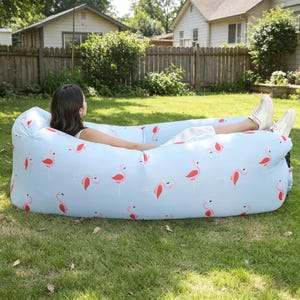 Pode incluir: Uma espreguiçadeira inflável com fundo azul claro e um padrão repetitivo de flamingos cor-de-rosa. O assento alongado e almofadado foi concebido para relaxar e é feito de um material leve e flexível.