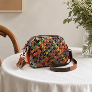 Peut inclure: Un sac à bandoulière en forme de dôme avec un extérieur en cuir tressé multicolore composé de bandes rouges, orange, jaunes, vertes et bleues. Le sac présente un panneau latéral en cuir marron, une fermeture éclair sur le dessus et une bandoulière.