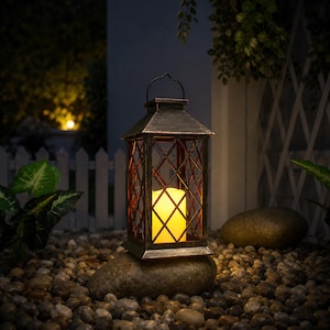 May include: A rectangular metal lantern with a dark, weathered bronze finish and a lattice frame design. The lantern features a top handle and contains a single, cylindrical, battery-operated LED candle that emits a warm, glowing yellow light.