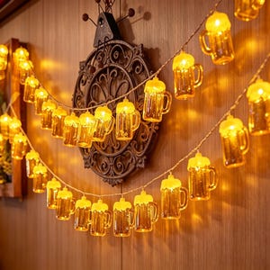 Puede incluir: Una cadena de luces LED con múltiples cubiertas pequeñas y translúcidas de color amarillo con forma de jarras de cerveza. Cada jarra brilla con una luz cálida, creando una iluminación festiva. La cadena cuelga en dos filas sobre una pared de madera.