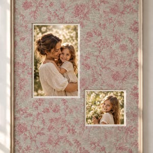 May include: A rectangular picture frame with a light wood finish and a matte featuring a pink floral toile pattern on a light gray background. The frame holds two photographs: one showing an adult and child embracing, and one showing a child holding flowers.