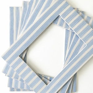 May include: A stack of rectangular picture frame mats featuring a light blue and white vertical striped pattern. Each mat has a clean, centered rectangular cutout with a white inner edge, arranged in a slightly offset, overlapping fan formation.