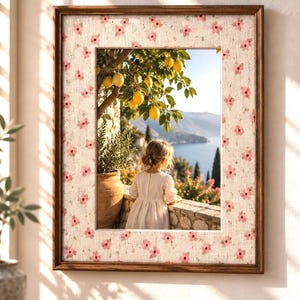May include: A rectangular wall frame with a dark wood border and a light-colored mat featuring a repeating pattern of small pink flowers. The frame displays a scene of a child looking out at a lemon tree and a coastal landscape.