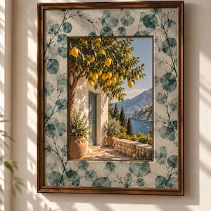 Könnte beinhalten: Ein rechteckiges Wandbild in einem dunkelbraunen Holzrahmen mit einem zentralen Bild eines Zitronenbaums neben einem Steingebäude mit Blick auf eine Küstenlandschaft, umgeben von einem Rand aus durchscheinenden blau-grünen Blattmustern.