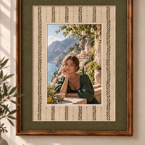 May include: A rectangular wall art piece featuring a dark wood frame and a wide olive green fabric mat. The inner border displays a cream-colored fabric with vertical rows of green leaf patterns. The central image shows a person in a green top.