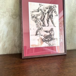 May include: A framed art print featuring a sepia-toned ink sketch of four figures in dynamic poses. The artwork is enclosed in a dark brown wooden frame with a deep red matting. The sketch depicts individuals in motion, with one figure seated.