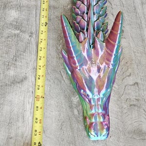 Könnte beinhalten: Eine bewegliche Drachenfigur mit metallisch irisierender Oberfläche in Grün-, Blau- und Violetttönen. Der Drache liegt neben einem gelben Maßband, das eine Gesamtlänge von etwa 216 Zentimetern anzeigt.