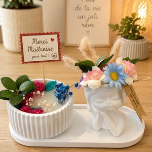 Peut inclure: Un bougeoir blanc cannelé avec des fleurs séchées roses et bleues et un panneau Merci Maîtresse pour tout, à côté d'un cache-pot blanc en forme de visage avec des fleurs artificielles, le tout sur un plateau ovale blanc.