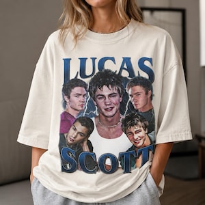 Puede incluir: Una camiseta de manga corta color blanco hueso con un estampado gr&aacute;fico del personaje Lucas Scott de One Tree Hill. El dise&ntilde;o incluye cinco retratos diferentes del personaje con el texto LUCAS SCOTT en letras azules grandes.