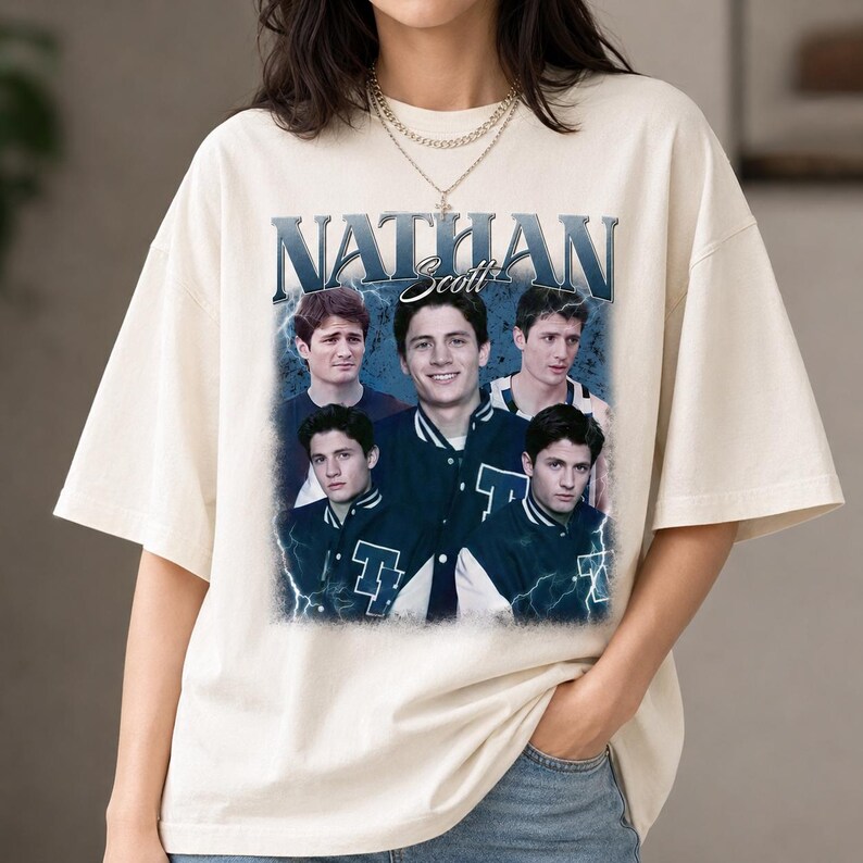 Puede incluir: Una camiseta de manga corta color hueso con un estampado gr&aacute;fico de Nathan Scott. El dise&ntilde;o incluye el texto NATHAN Scott en una fuente negrita sobre varias im&aacute;genes de la misma persona con una chaqueta universitaria sobre un fondo de rayos azules.