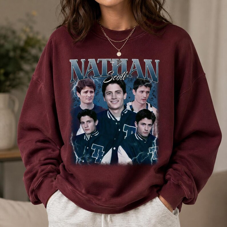 Puede incluir: Una sudadera de cuello redondo color granate con un estampado gr&aacute;fico de Nathan Scott. El dise&ntilde;o incluye varias im&aacute;genes del personaje con una chaqueta universitaria, sobre un fondo azul con rayos y el texto NATHAN Scott en letras negritas.