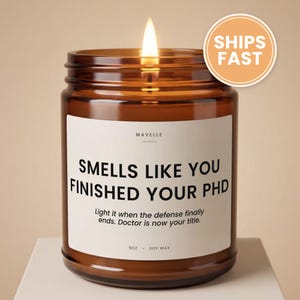 May include: A lit candle in an amber glass jar with a white label that reads MAVELLE, SMELLS LIKE YOU FINISHED YOUR PHD, Light it when the defense finally ends. Doctor is now your title., 9oz, SOY WAX. The candle has a single burning wick.
