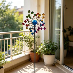 May include: A kinetic garden spinner featuring a central blue sphere with radiating metal arms, each tipped with a small, colourful, translucent orb in shades of red, orange, yellow, green, blue, and purple, mounted on a tall black metal pole.