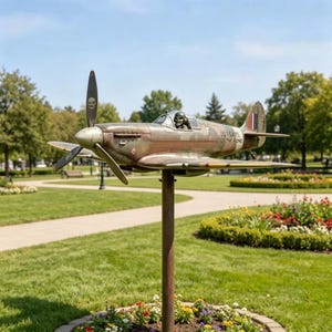 May include: A metal sculpture of a vintage fighter airplane mounted on a tall pole. The plane features a camouflage paint scheme, a propeller with a skull emblem, and a pilot figure in the cockpit. The text 50 YEARS OF THE SONG is visible.