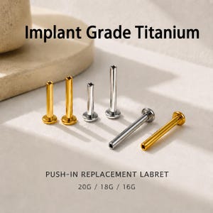Op de afbeelding: Een collectie van goud- en zilverkleurige push-in vervangende labretstaafjes van implantaat-titanium. De afbeelding bevat de tekst Implant Grade Titanium, PUSH-IN REPLACEMENT LABRET en 20G / 18G / 16G, met verschillende lengtes en afwerkingen.