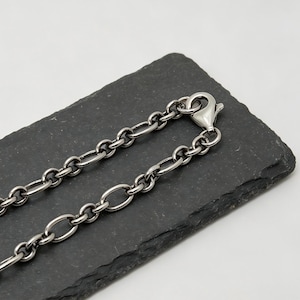 May include: A dark silver-toned metal chain necklace featuring a series of uniform oval links connected in a continuous pattern. The chain is secured with a small, functional lobster claw clasp at one end, showcasing a polished metallic finish.