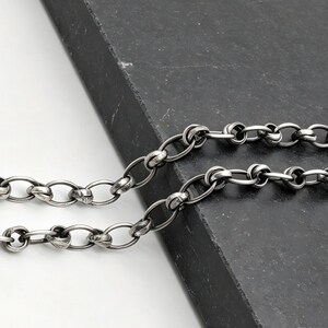 May include: A dark silver-toned chain necklace featuring a series of interconnected oval links with a textured, oxidised finish. The chain includes a secure lobster claw clasp at one end, showcasing a uniform link design throughout the entire piece.