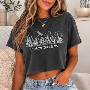 May include: A charcoal gray short-sleeved t-shirt featuring a white line art graphic of various insects playing musical instruments, including a dragonfly, beetle, and grasshopper. The text Custom Text Here is printed below the insect illustration.