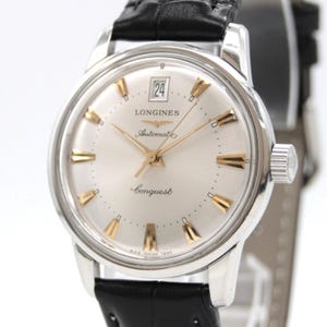 May include: A Longines Conquest automatic wristwatch with a silver dial, gold-tone hour markers, and a date window at the twelve o'clock position. The watch features a polished silver-tone stainless steel case and a black leather strap.