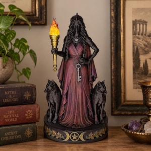 May include: A statue of a dark-haired figure in a flowing burgundy gown, holding a golden torch with a bright orange flame. The figure wears a necklace with a key pendant and stands between two black wolves on a circular base with a triple moon symbol.
