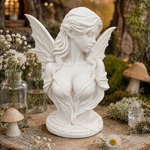May include: A white matte finish bust sculpture of a winged figure with long flowing hair and pointed ears. The figure wears a draped garment with a low neckline and intricate leaf-like textures. The sculpture is depicted from the chest up.