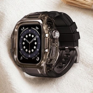 May include: A smartwatch featuring a dark, translucent, smoke-colored protective case and a black silicone strap. The watch face displays a circular digital interface with white markers, numbers, and a central clock display with thin hands.