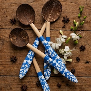 May include: Three spoons with dark brown textured coconut shell bowls and light wooden handles. The lower portion of each handle features a vibrant blue and white marbled pattern. The spoons are arranged in a cluster alongside star anise.