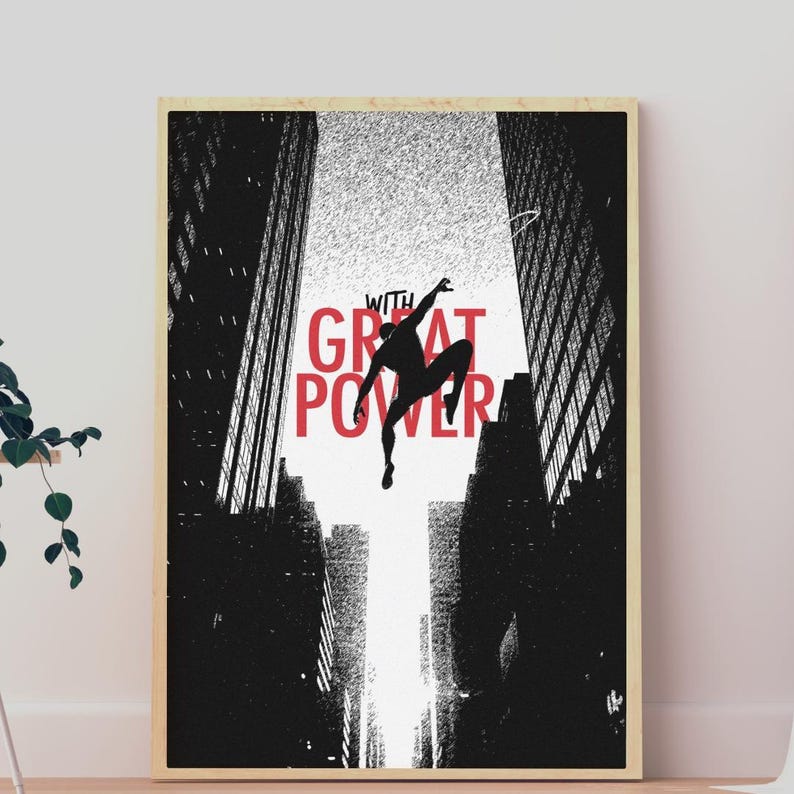 May include: A rectangular wall art print in a light wood frame featuring a black silhouette of a figure leaping between two tall, dark, textured city buildings. The text "WITH GREAT POWER" is printed in bold red letters behind the figure.