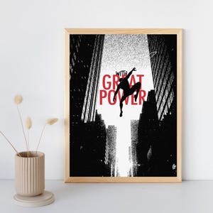 May include: A framed wall art print featuring a black silhouette of a figure leaping between two tall, textured black and white buildings. The text "WITH GREAT POWER" is printed in bold red capital letters across the center of the image.